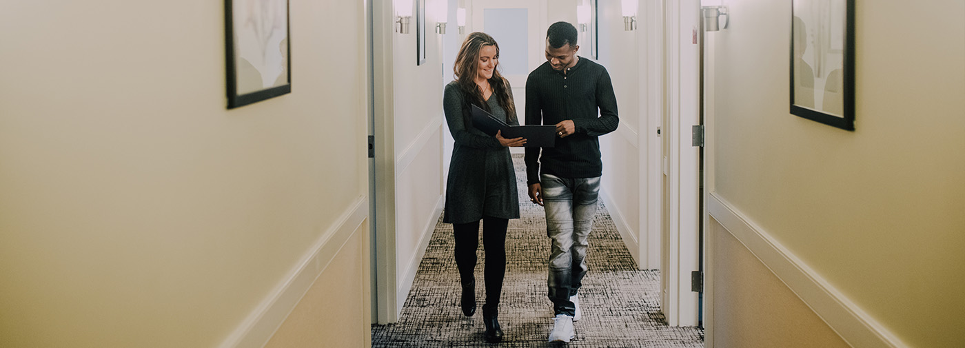 man and woman reading notepad walking down a hallway